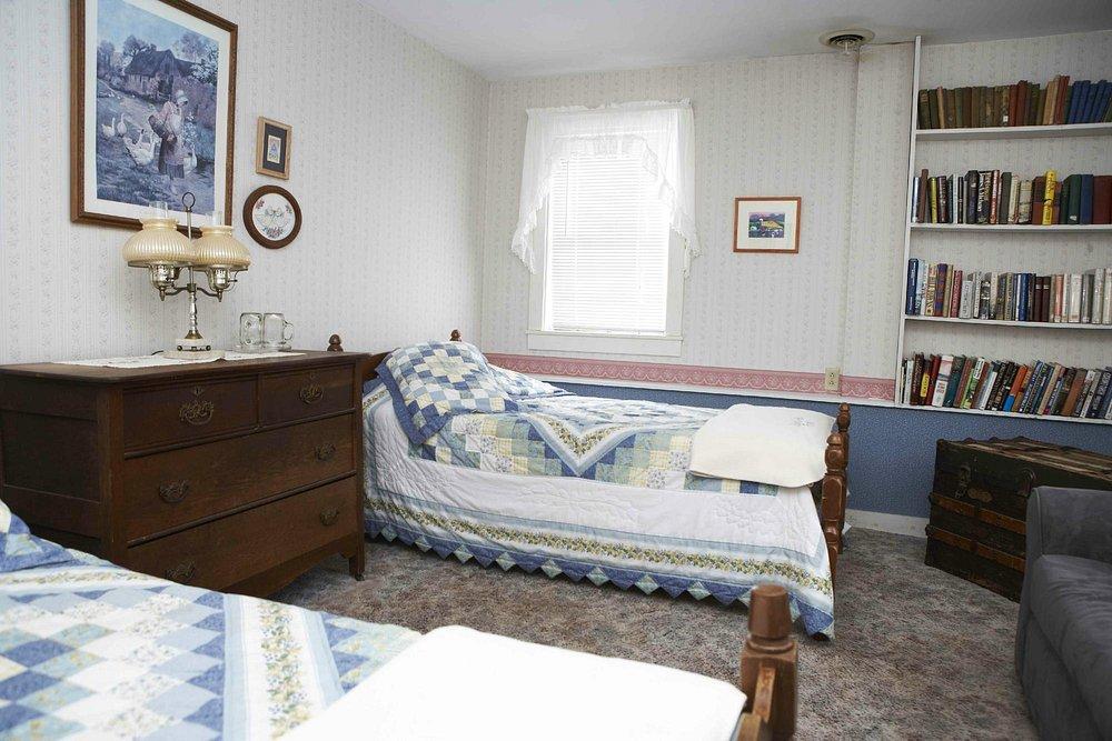 Cozy bedroom with two single beds, bookshelves, dresser, and framed artwork.