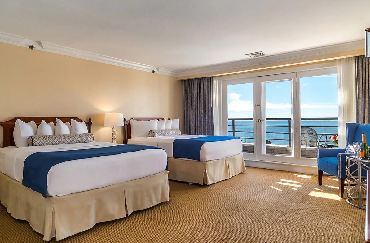 Two beds in a hotel room with ocean view balcony.