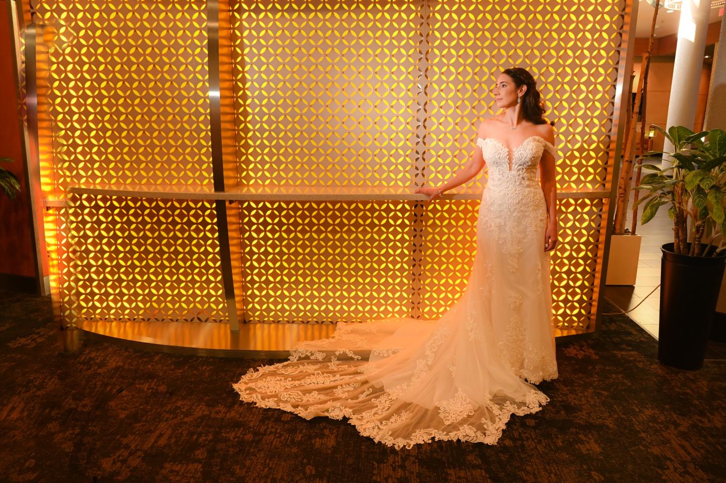 Bride in a flowing white gown stands by a golden lit wall.
