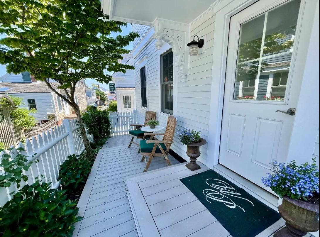 Charming porch with chairs, small tables, and potted plants under a sunny sky.