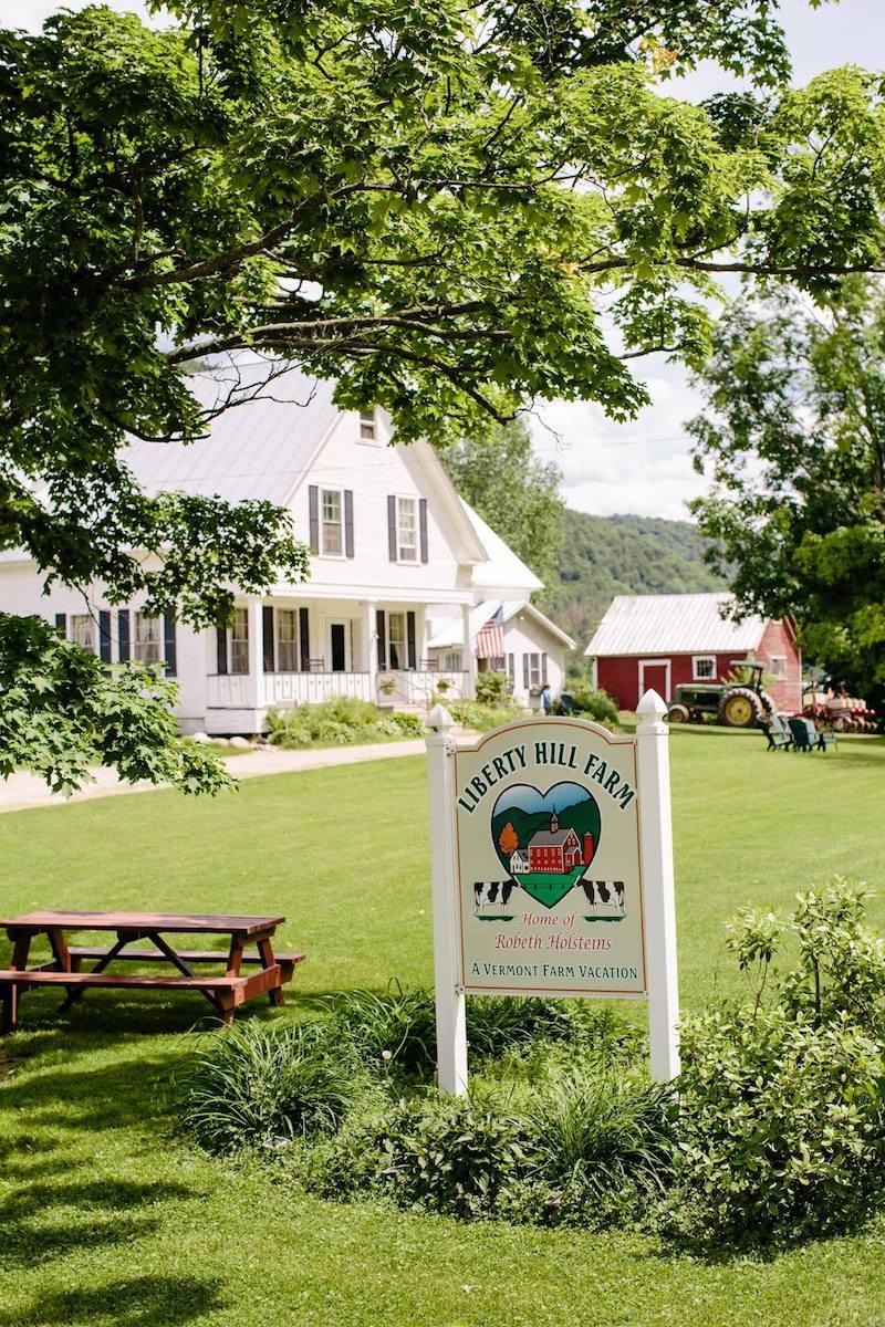 White house with a yard sign, surrounded by trees and a picnic table on a sunny day.