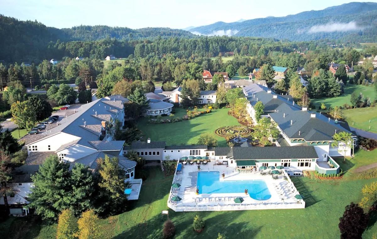 Hotel complex with pool, surrounded by green lawns and forested hills.