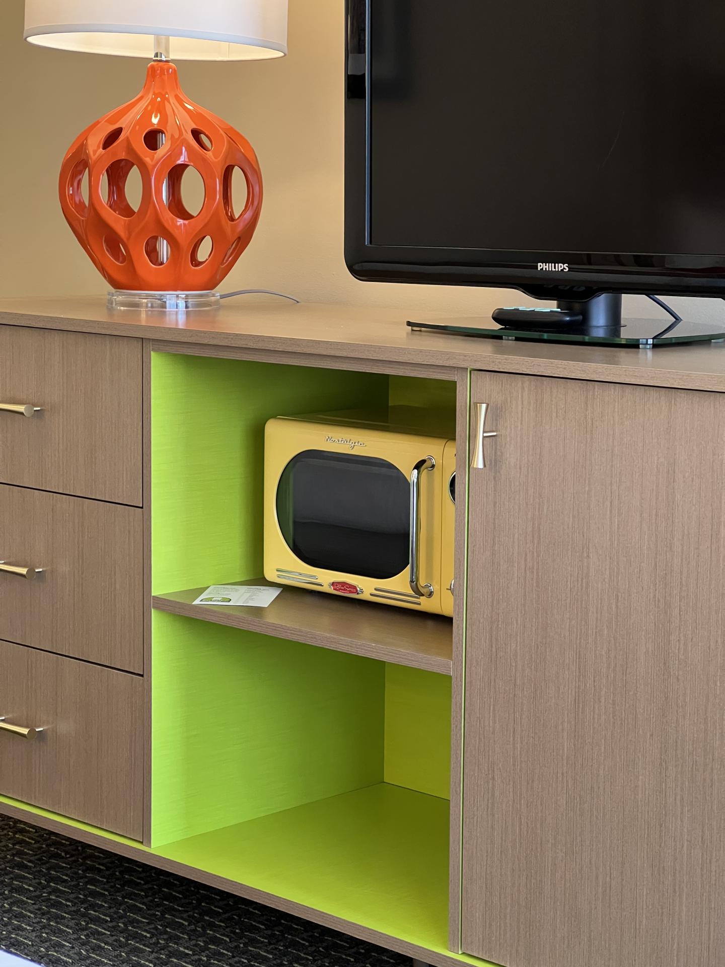 Modern cabinet with TV, orange lamp, and small yellow microwave.
