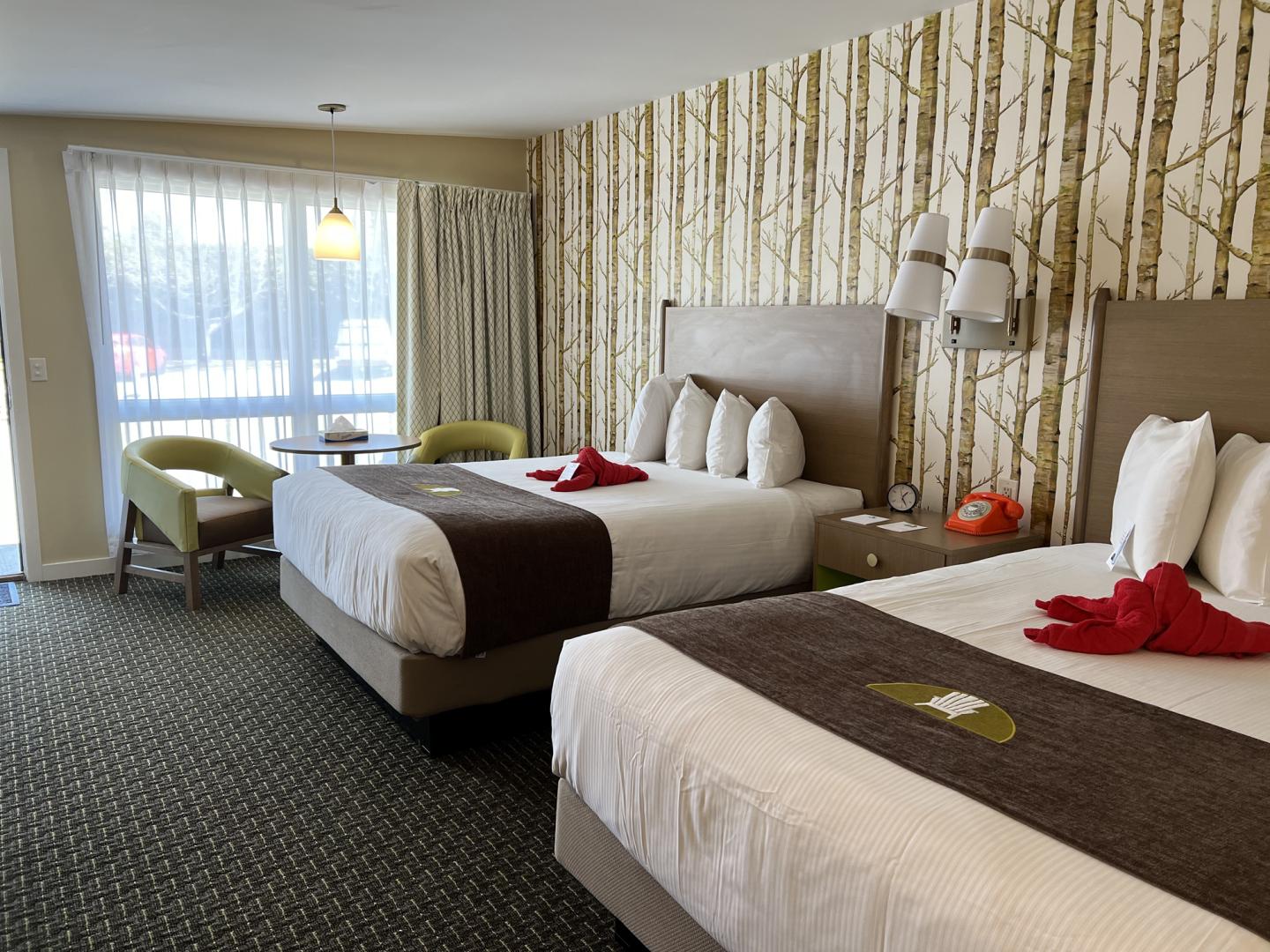 Hotel room with two beds, woodland wallpaper, and a window.