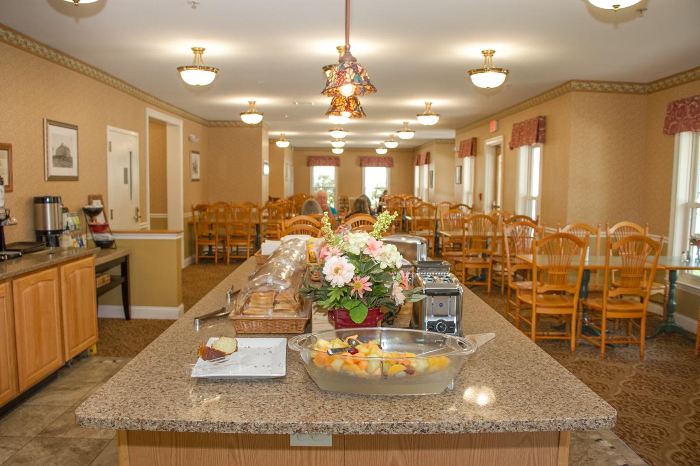 Dining area with long tables, chairs, and food on a central counter.