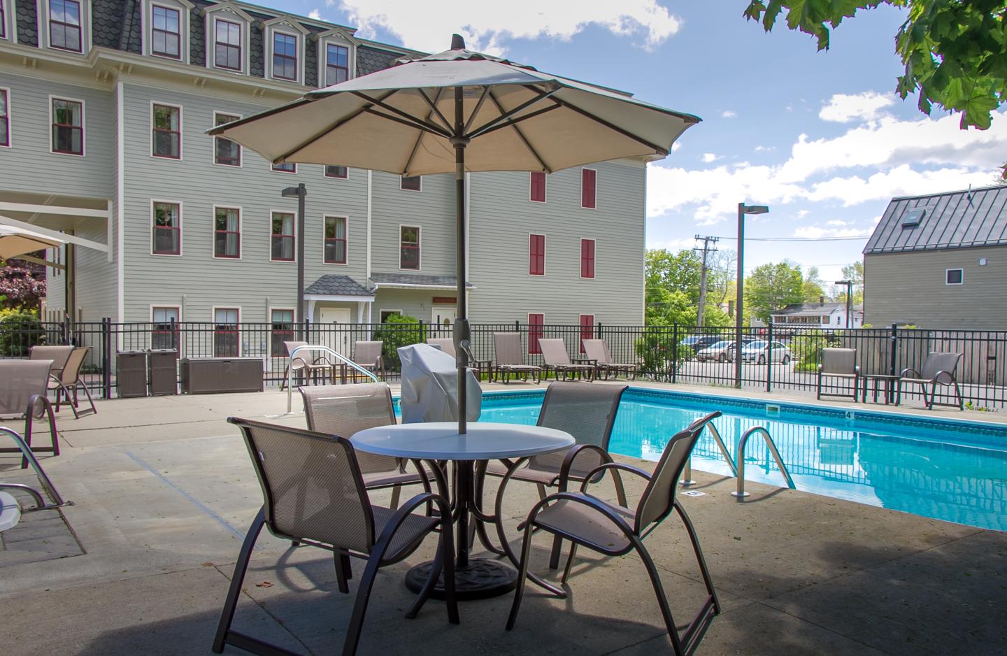 Patio with umbrella table by a swimming pool, near a multi-story building.