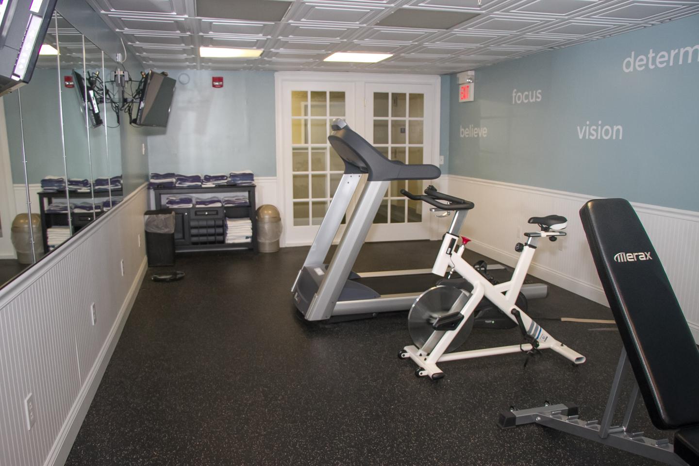 Small gym with treadmill, stationary bike, and bench on a rubber floor.