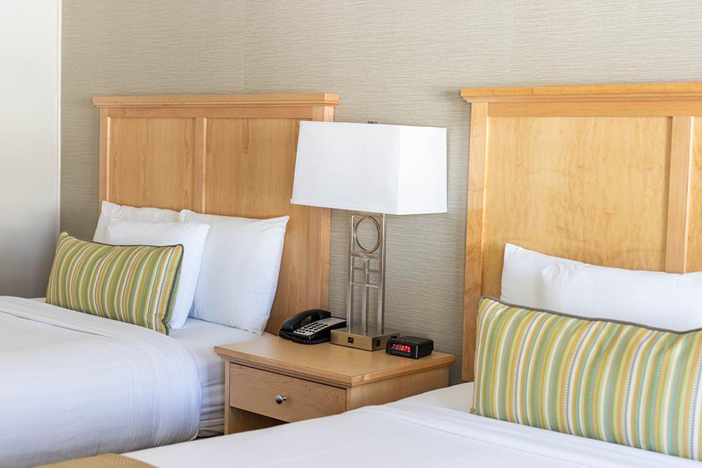 Two neatly made beds with striped pillows, separated by a nightstand and lamp.
