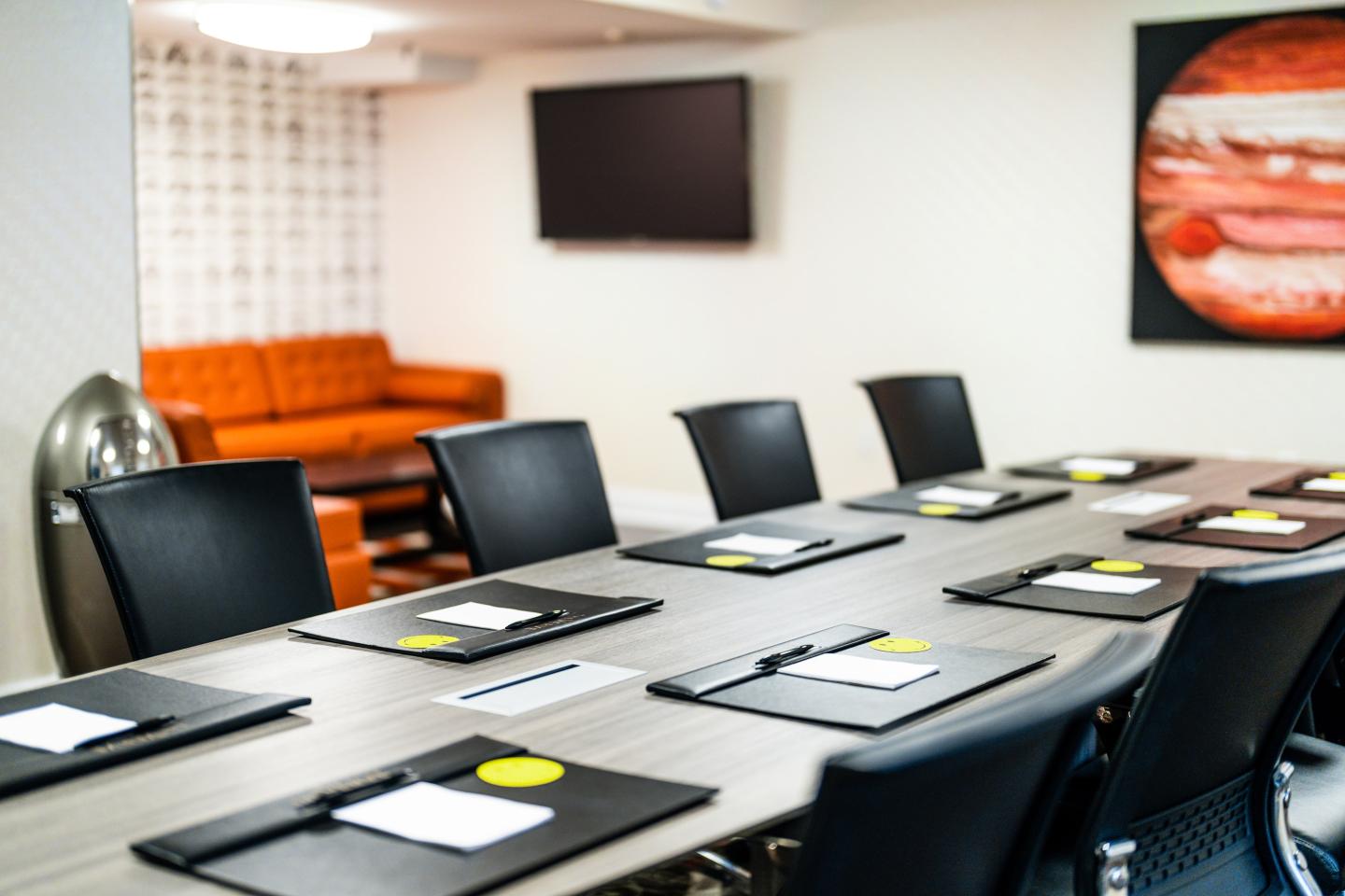 Meeting room with chairs, table set with folders, and orange couch in the background.