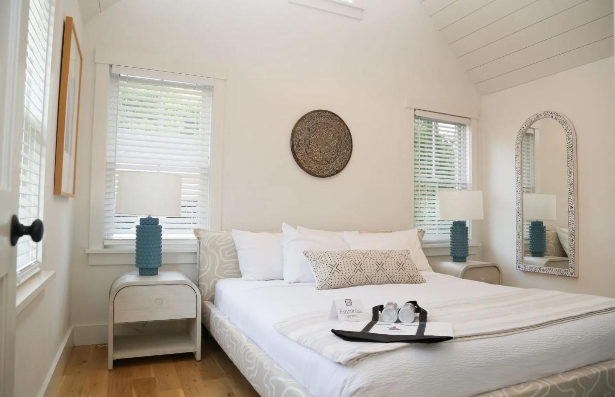 Cozy white bedroom with large bed, blue lamps, and decorative wall mirror.