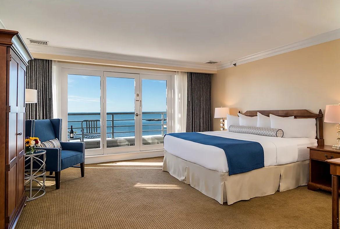 Hotel room with ocean view, large windows, and a blue-accented bed.