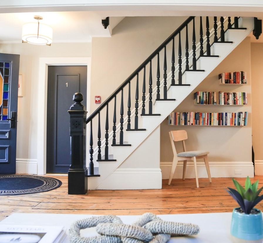 Staircase with black railings, bookshelves underneath, wooden floor, and blue door.