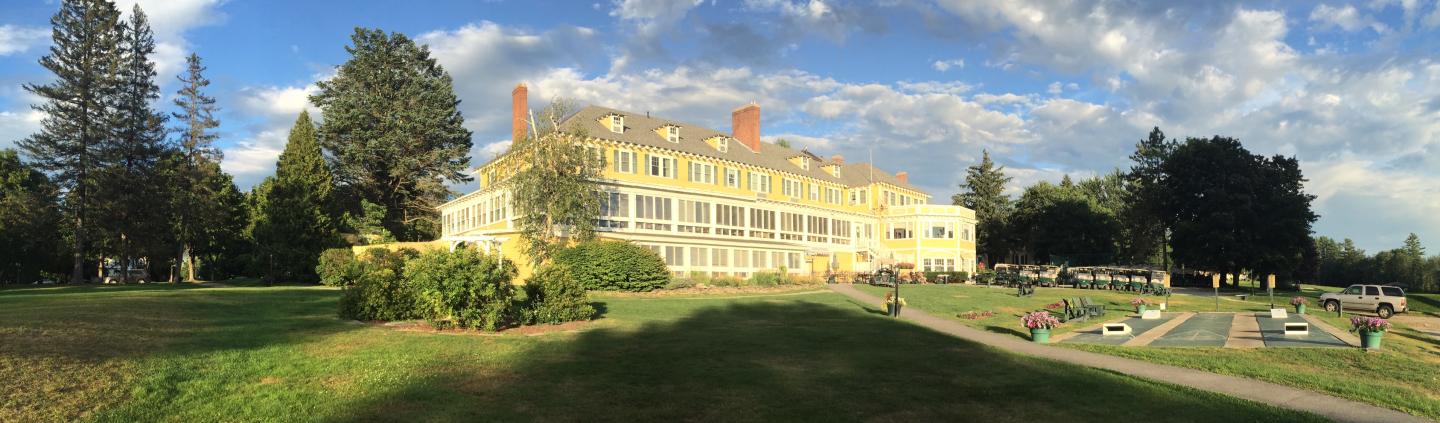 Yellow mansion with chimneys, trees, and blue sky with clouds.