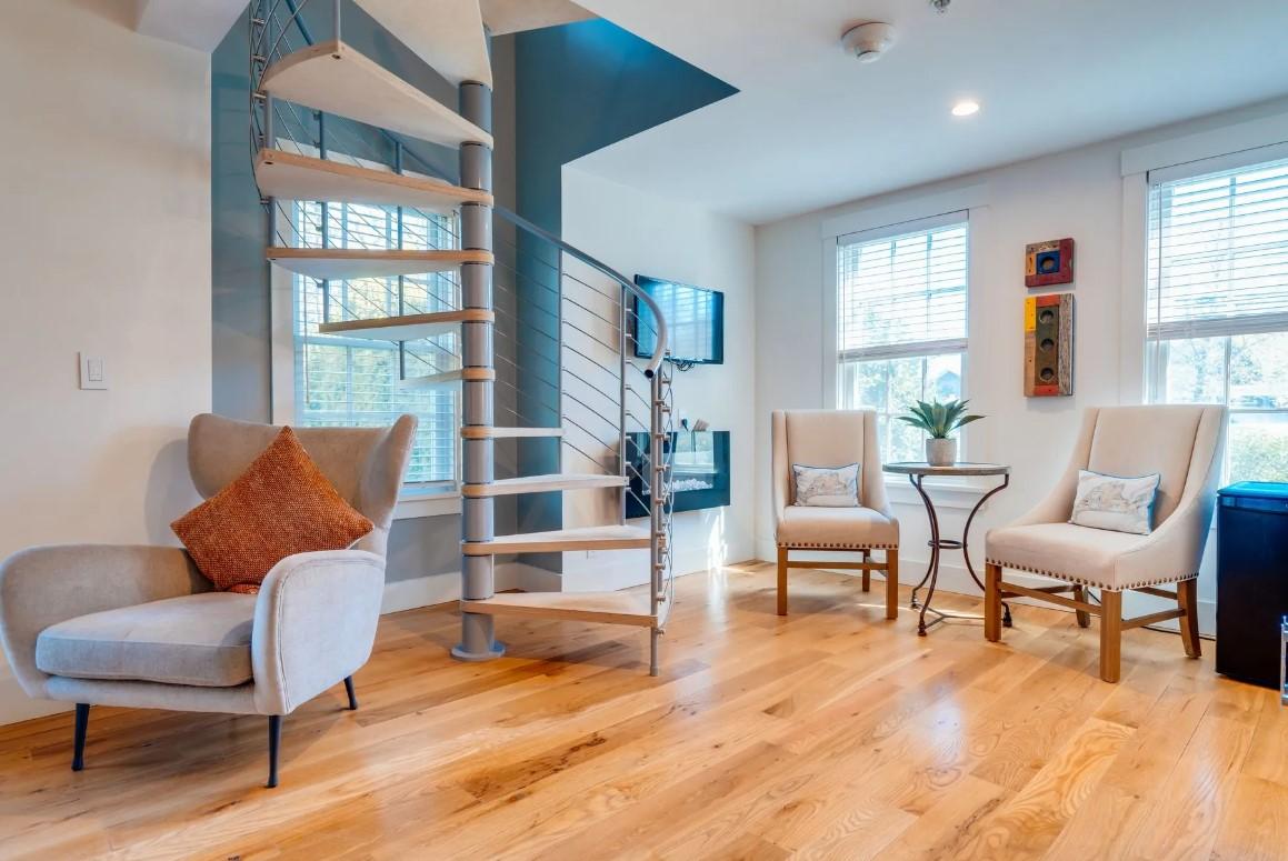 Spiral staircase in a modern living room with wooden floors and armchairs.
