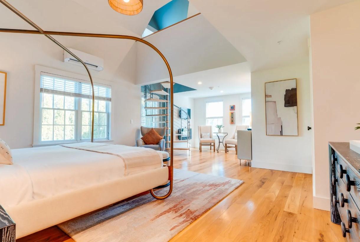 Spacious bedroom with hardwood floors, large bed, and bright windows.