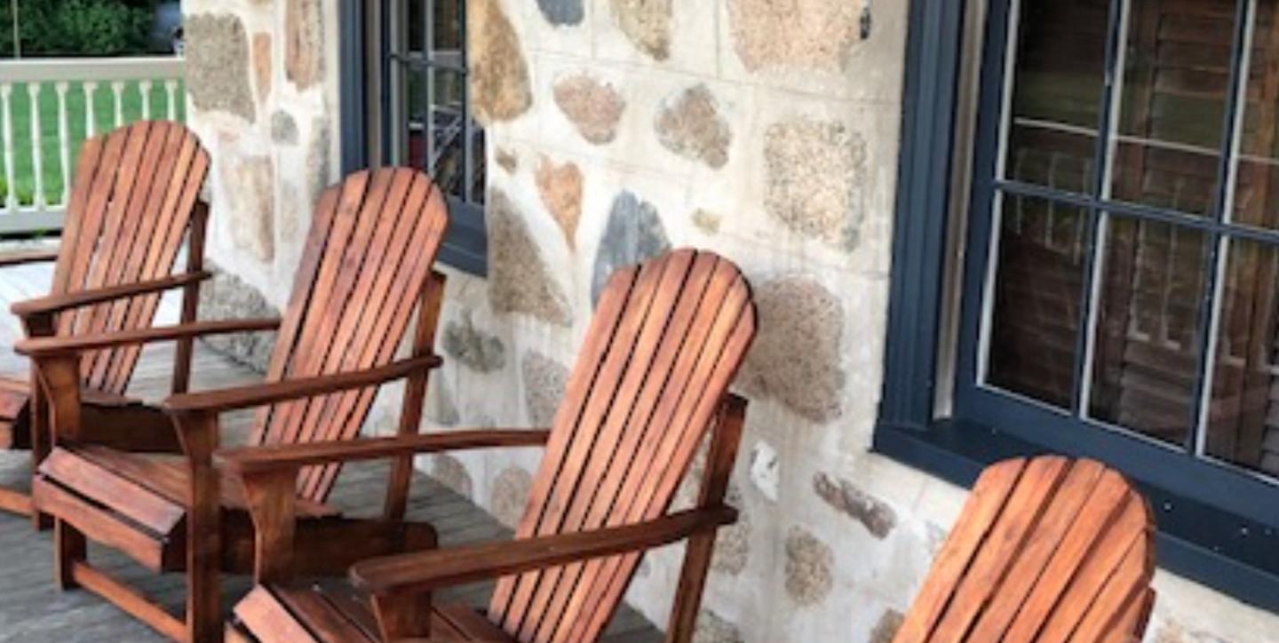 Three wooden chairs on a porch against a stone wall.