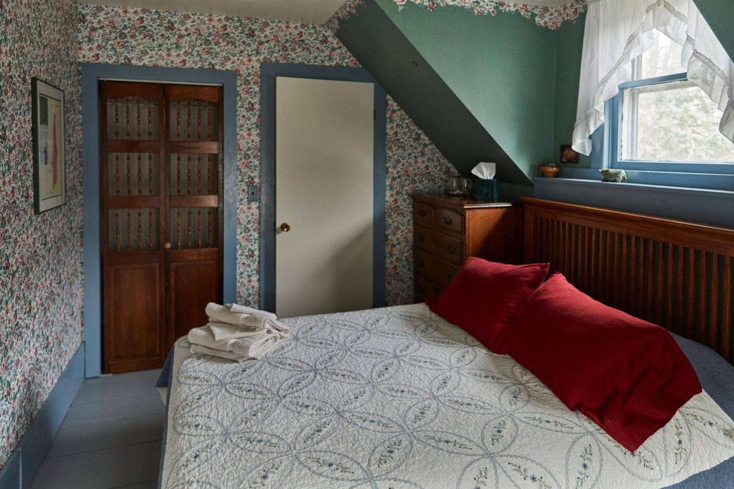 Cozy bedroom with floral wallpaper, red pillows, and a wooden door.