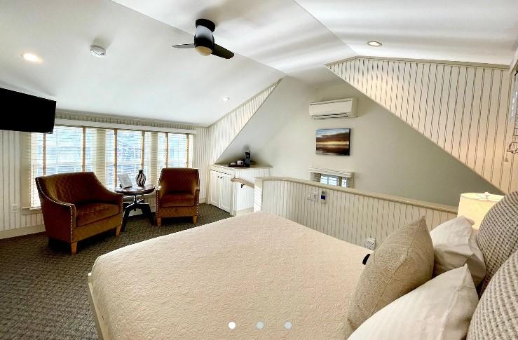 Cozy attic bedroom with chairs, large bed, and windows.