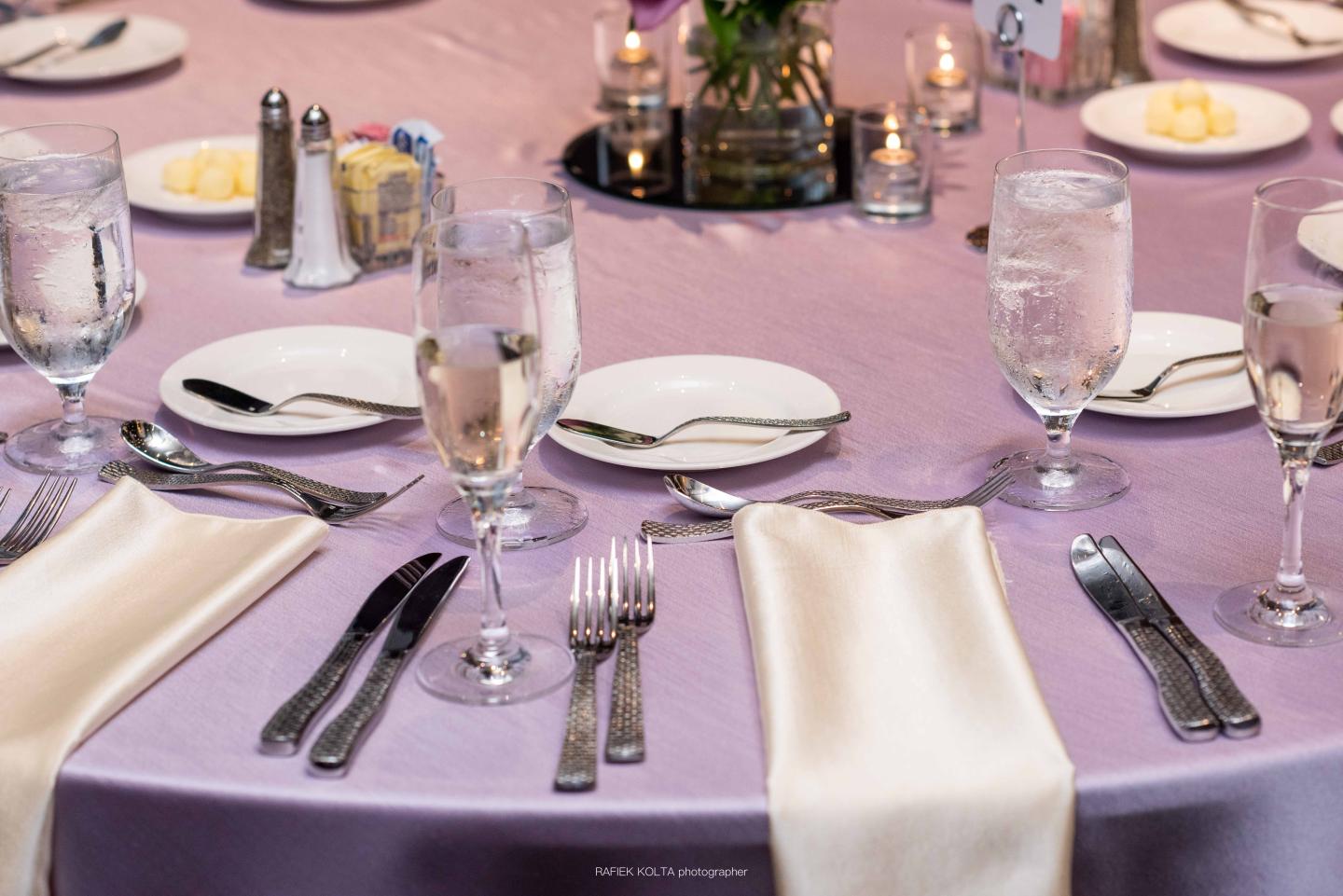 Elegant table setting with lilac cloth, glassware, and white napkins.