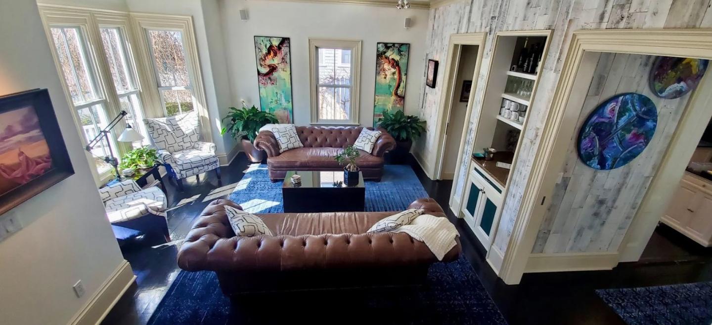 Cozy living room with brown sofas, stained glass art, plants, and a blue rug.