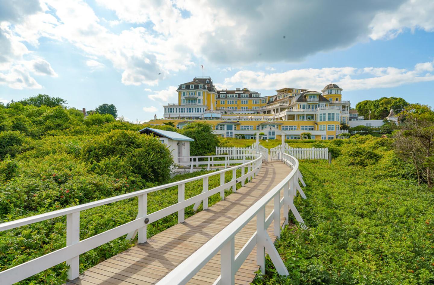 Wooden boardwalk leads to a large yellow hotel under a partly cloudy sky.