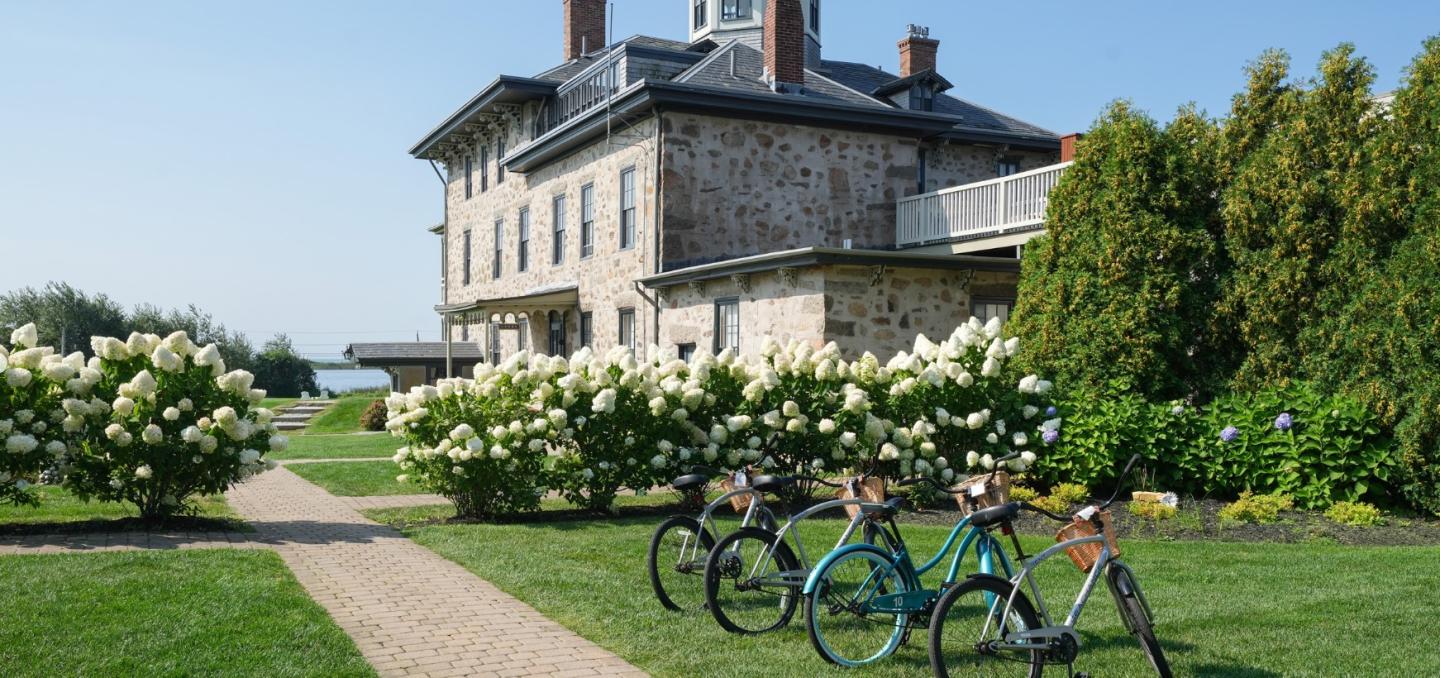 Stone house with a garden path, bicycles, and blooming flowers under a clear blue sky.