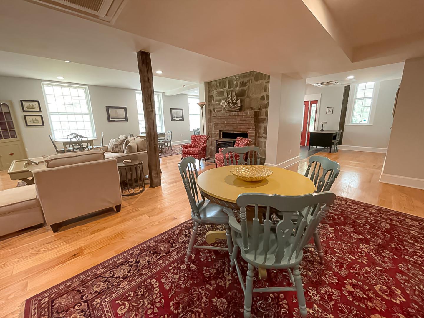 Dining area with a round table and chairs on a red patterned rug. Cozy living room in the background.