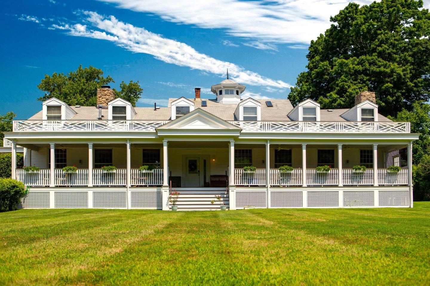Historic white house with a wide porch, set against a blue sky and green lawn.