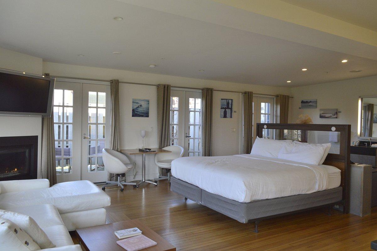 Spacious hotel room with a bed, seating area, and desk, featuring large windows.