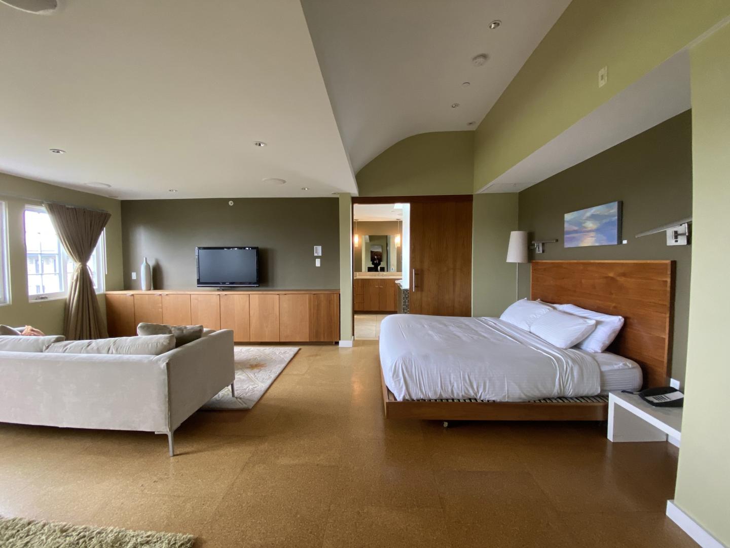 Spacious modern bedroom with a bed, sofa, and flat-screen TV. Cream and green tones.