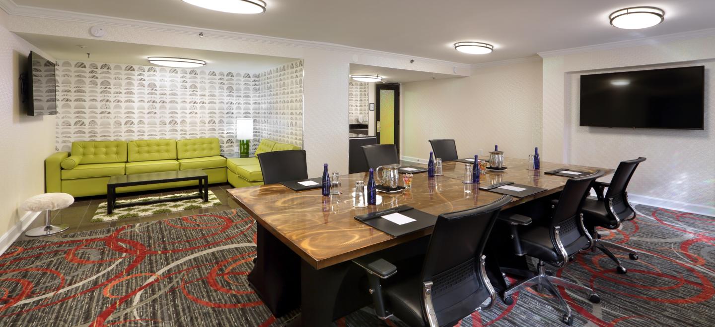 Modern meeting room with a table, chairs, a green sofa, and a large TV