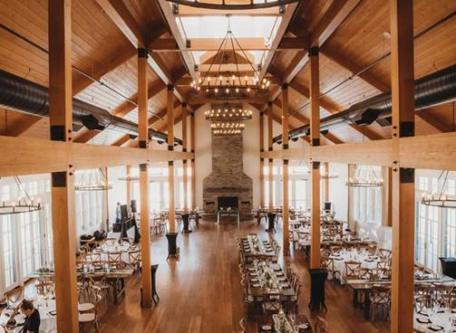 Spacious banquet hall with wooden beams and elegant chandeliers.