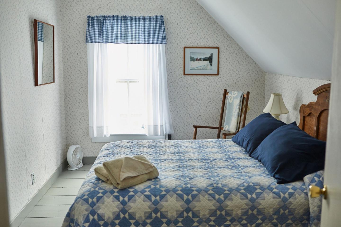 Cozy bedroom with blue quilt, matching curtains, and soft lighting.