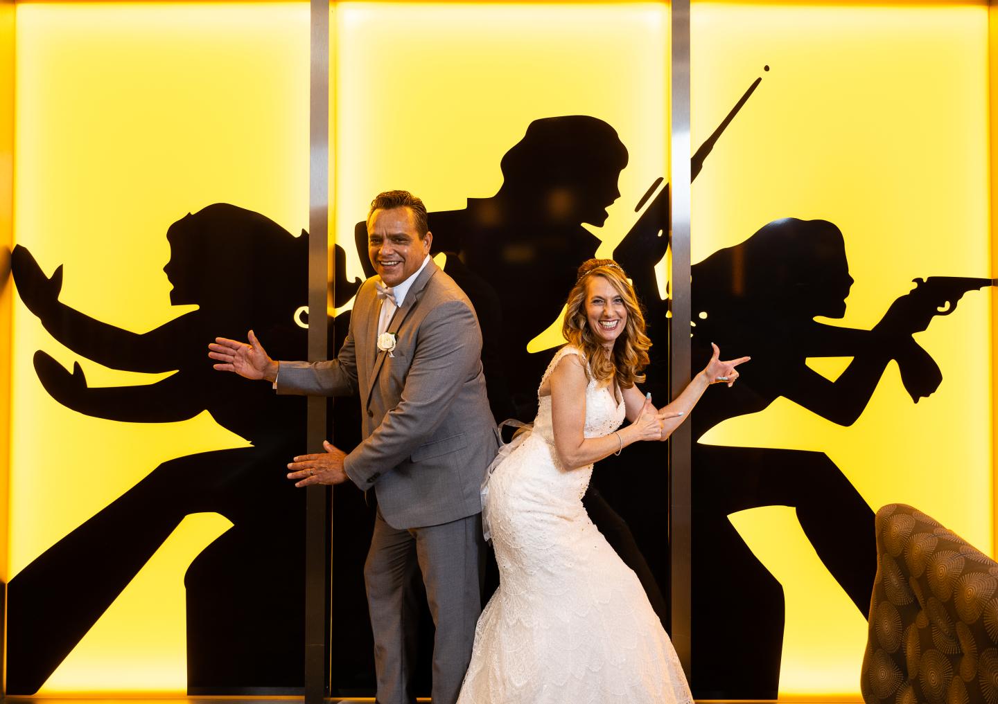 Bride and groom posing playfully in front of silhouettes on a yellow background.