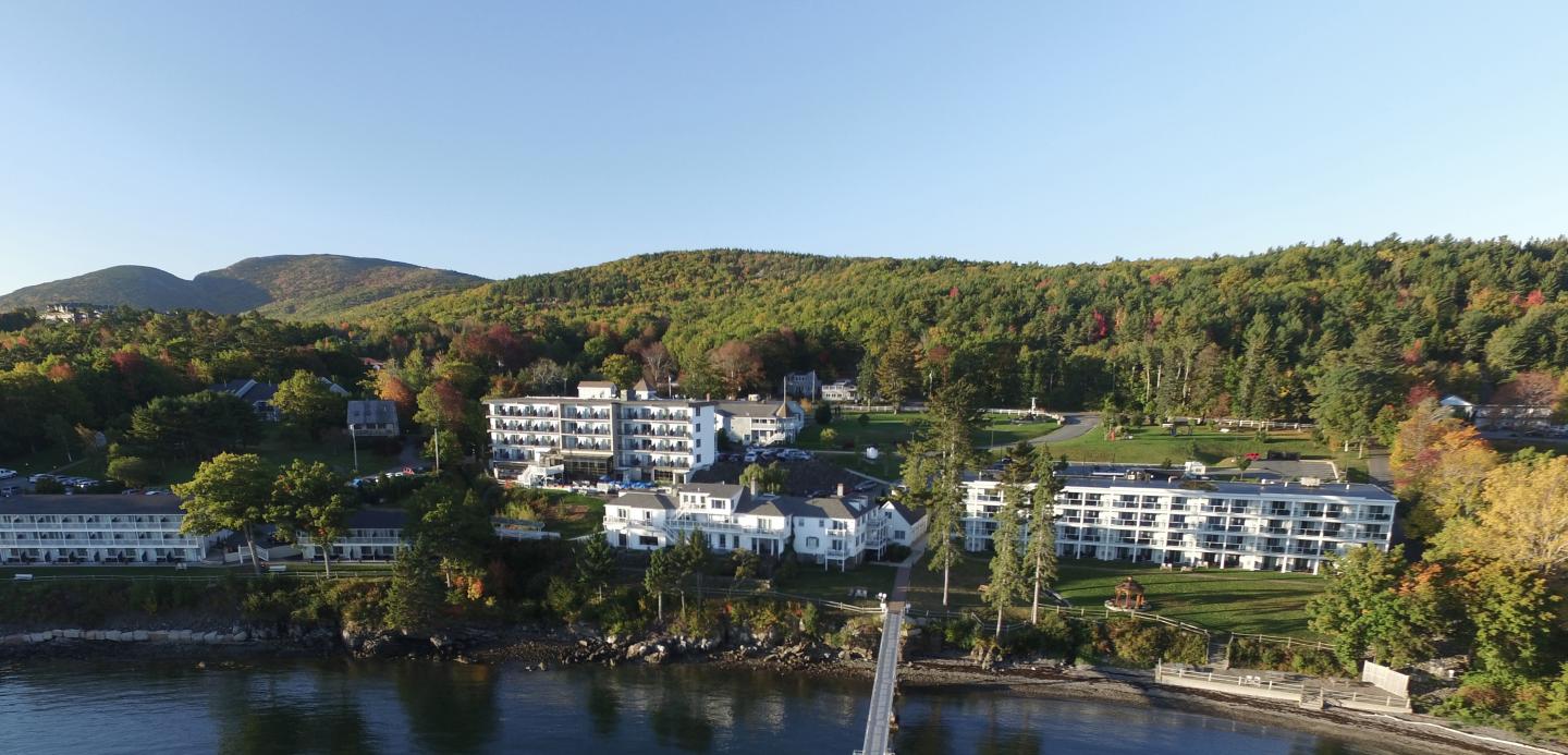 Resort by a lake with forested hills in the background, under a clear blue sky.