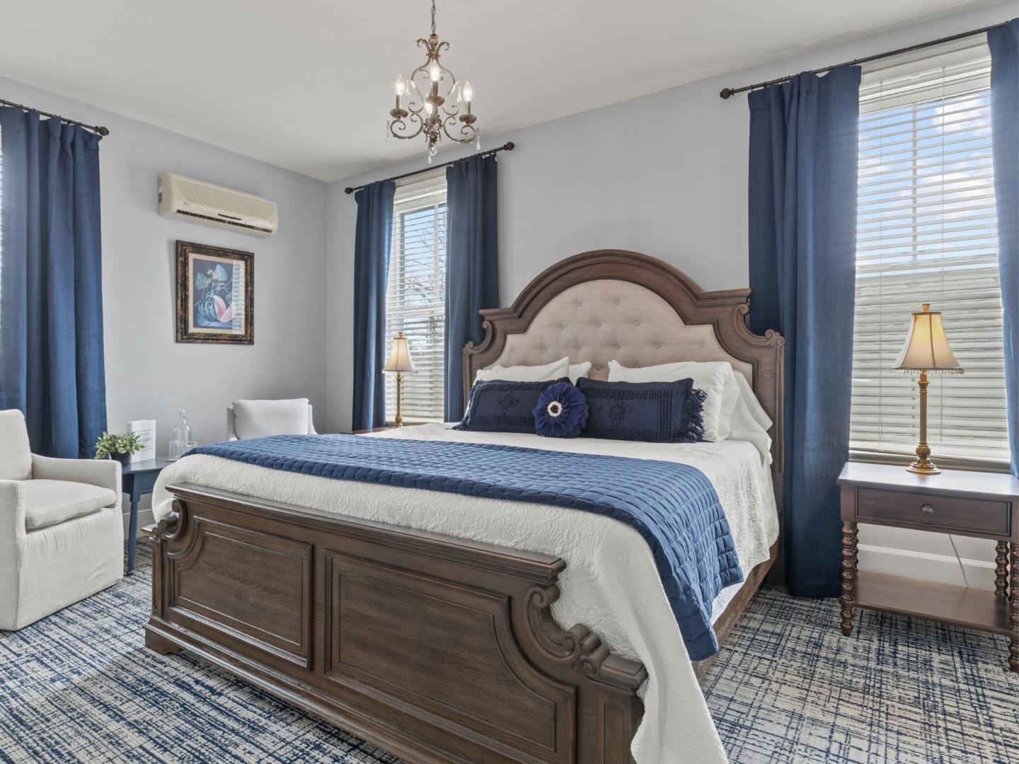 Elegant bedroom with a large wooden bed, blue accents, and two windows with curtains.
