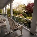 Covered porch with rocking chairs, overlooking a garden with blooming trees.