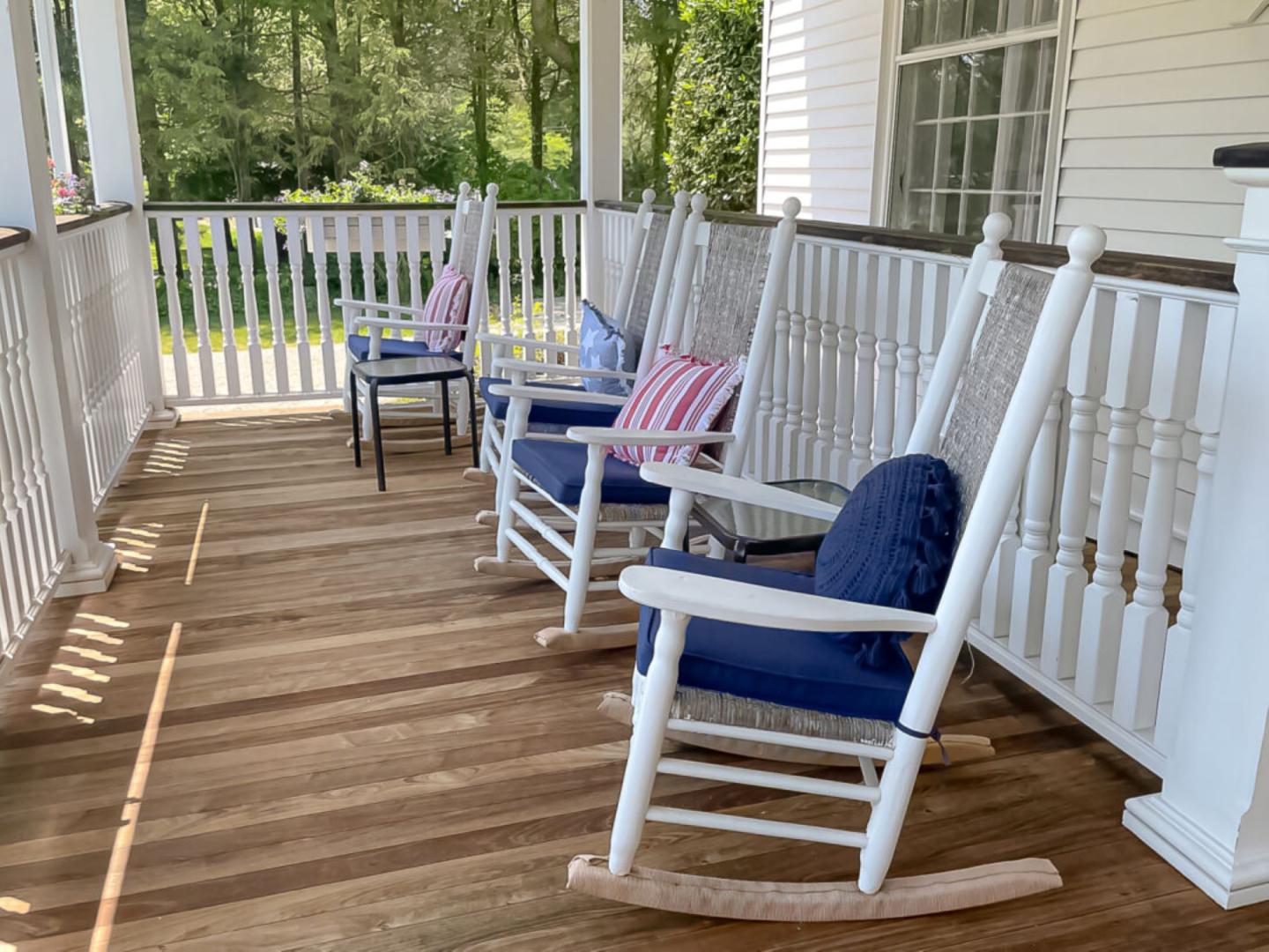 White rocking chairs on a wooden porch with cushions and a green view.