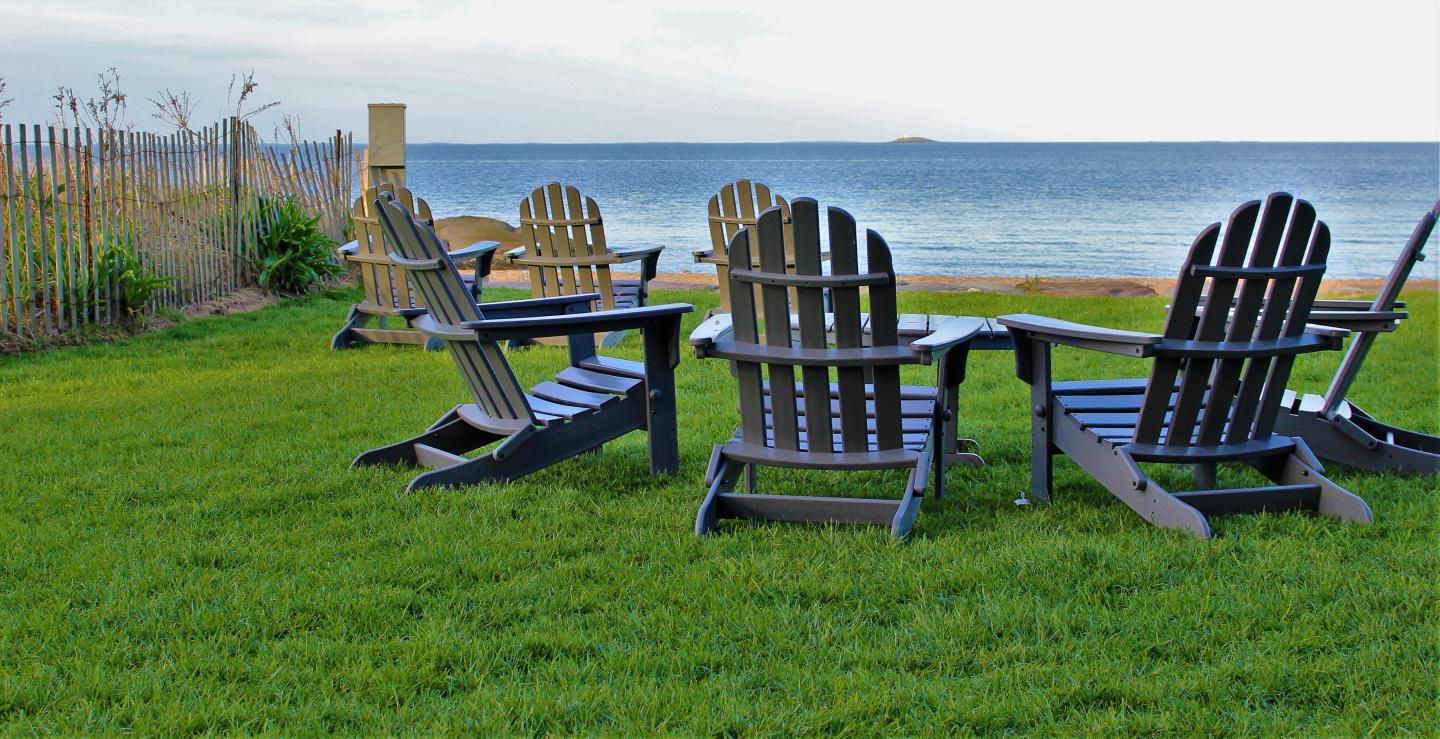 Chairs on a grassy shore facing a calm sea.