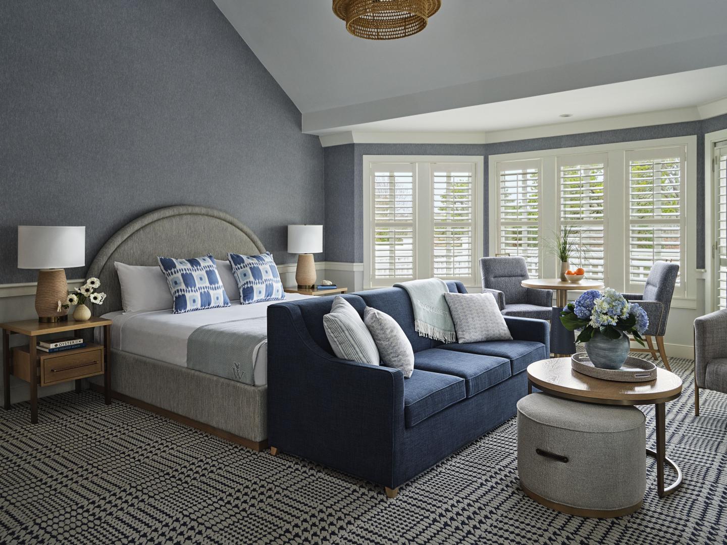 Spacious bedroom with blue sofa, bed, and large windows.