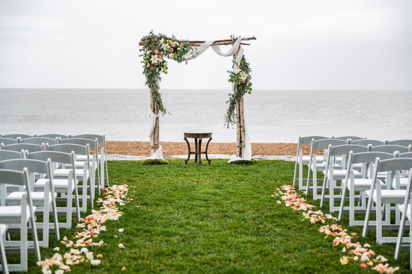Beachfront wedding arch with floral decorations and white chairs.