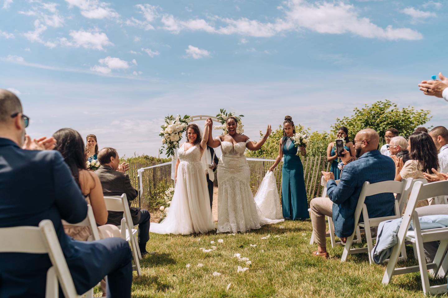 Brides holding hands, celebrating outdoors at a wedding ceremony.