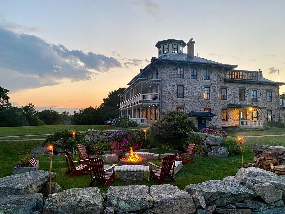 Stone house at sunset with lit firepit and outdoor seating.pit