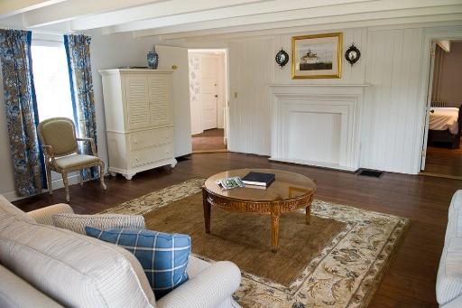Cozy living room with vintage furniture, white walls, and patterned curtains.Gatehouse