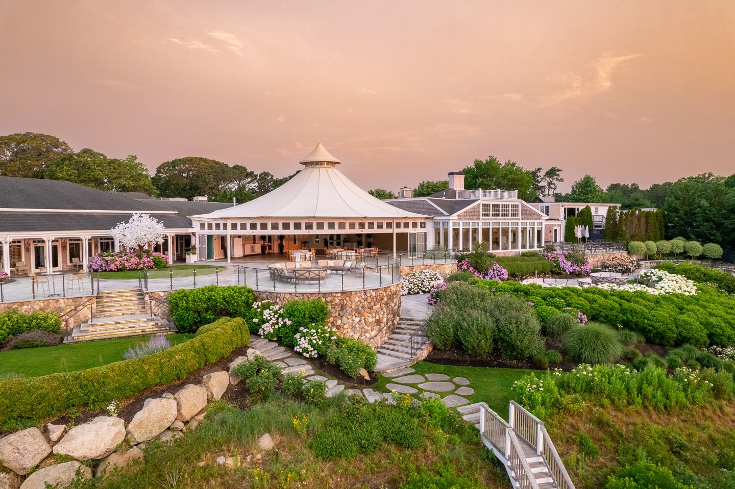 Elegant building with a glass dome, lush gardens, and a warm evening sky.