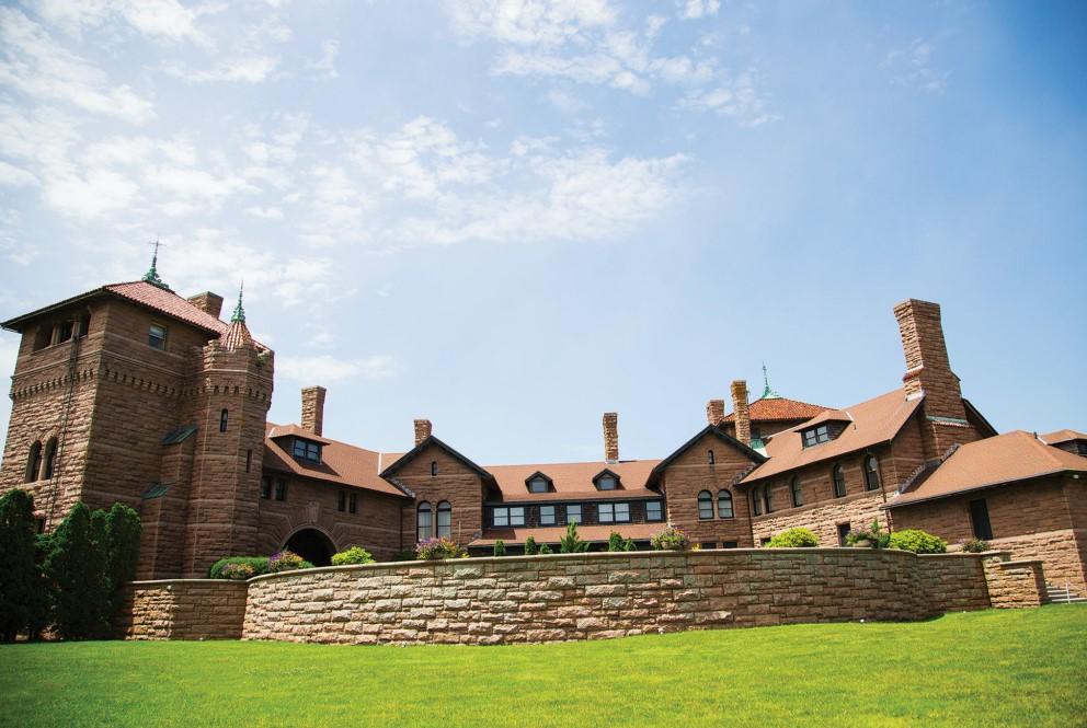 Historic mansion with red brick, green lawn, clear sky.