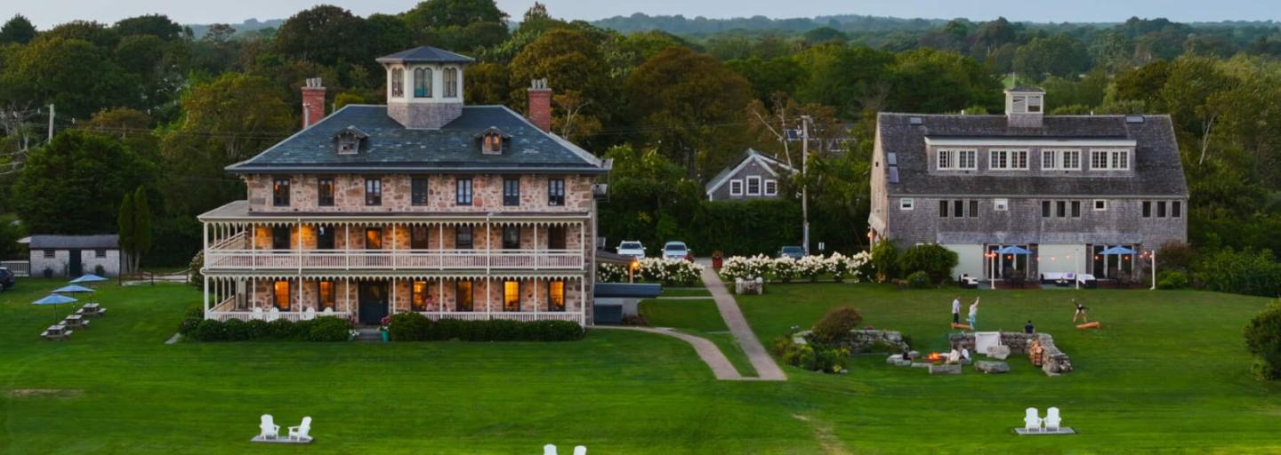 Historic estate with large lawns and two lit-up colonial-style buildings at dusk.