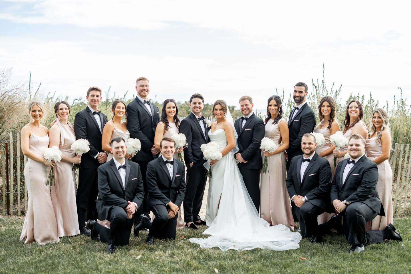 Wedding party outside, women in light dresses, men in dark suits, smiling.