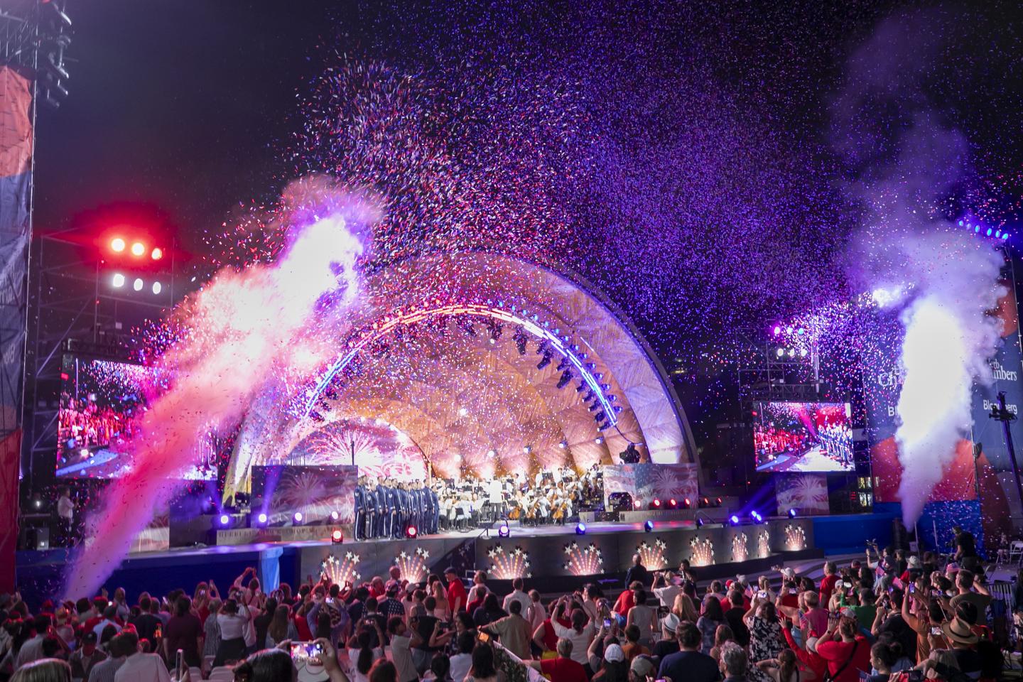 Concert with colorful lights, fireworks, and a cheering crowd at night.