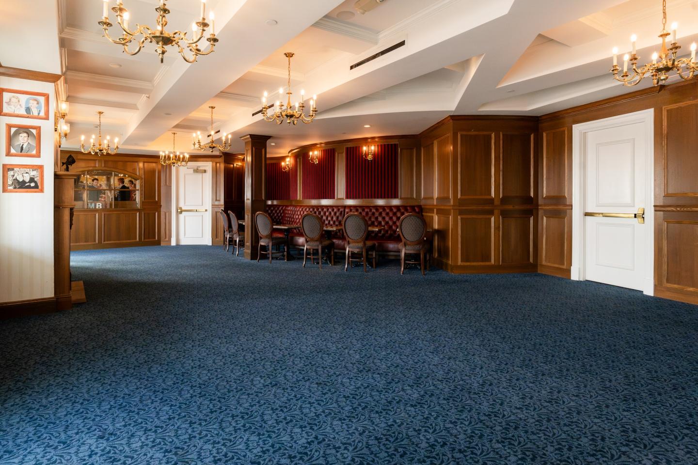 Elegant room with chandeliers, blue carpet, and wood paneling, with a small table and chairs.